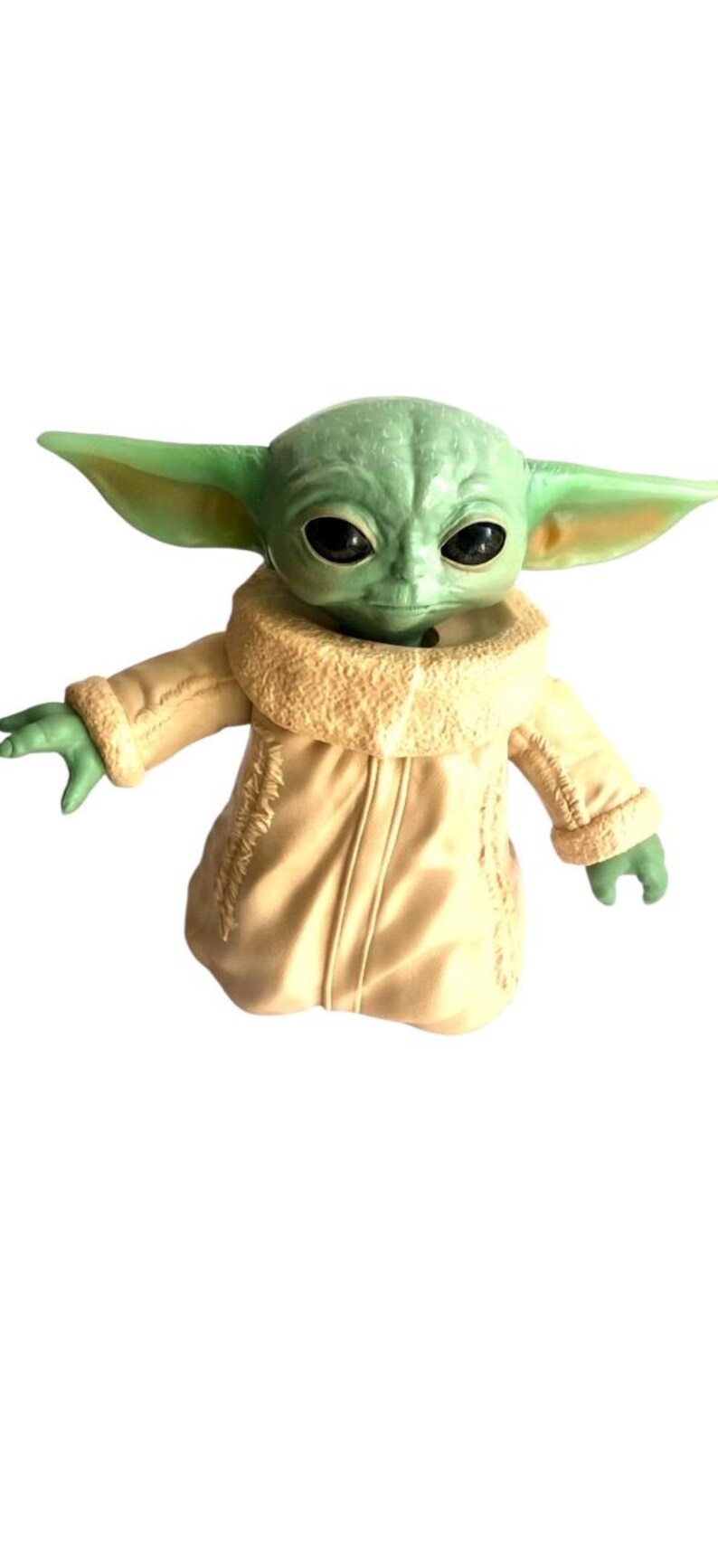 May include: A green and brown plush toy of a character from the Star Wars franchise, wearing a cream-colored jacket with a fur collar.