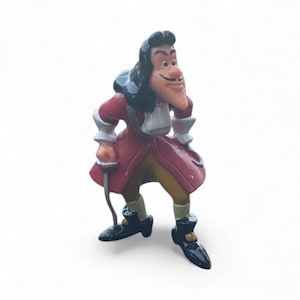 May include: A figurine of Captain Hook, a character from Peter Pan. The figure is dressed in a red coat, yellow pants, and black boots. He has a black wig, a long nose, and a mustache. He is holding a sword.