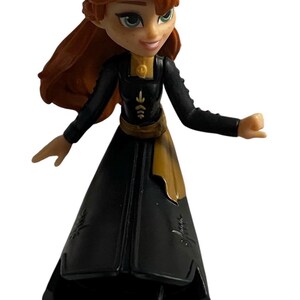 May include: A small plastic figurine of Anna from the movie Frozen wearing a black dress with gold accents and a gold belt. Her hair is long and red.