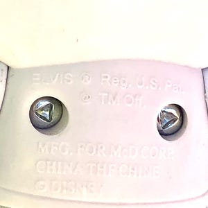 May include: White plastic toy figurine of Elvis Presley with the text "ELVIS Reg. U.S. Pat. @TM Of MFG. FOR McD CORE CHINA THE CHINE DISNEY" on the bottom.