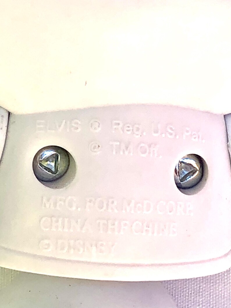 May include: White plastic toy figurine of Elvis Presley with the text "ELVIS Reg. U.S. Pat. @TM Of MFG. FOR McD CORE CHINA THE CHINE DISNEY" on the bottom.