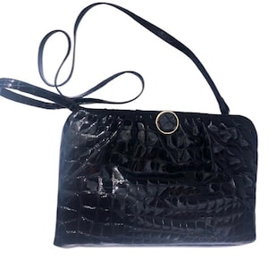 May include: A black crocodile-embossed leather handbag with a gold-toned clasp. The bag has a long strap for shoulder carrying.