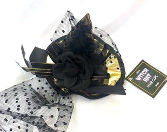 Puede incluir: Pinza para el pelo con forma de sombrero de bruja negro y dorado con red de lunares negros y un acento de flor negra. El empaque dice "Mini Witch Hat Hair Clips".