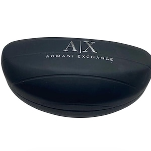 Może przedstawiać: Czarne, owalne etui na okulary przeciwsłoneczne. Etui ma matowe wykończenie i srebrny napis "AX ARMANI EXCHANGE" na górze. Etui jest zamknięte i wydaje się być wykonane z wytrzymałego materiału.