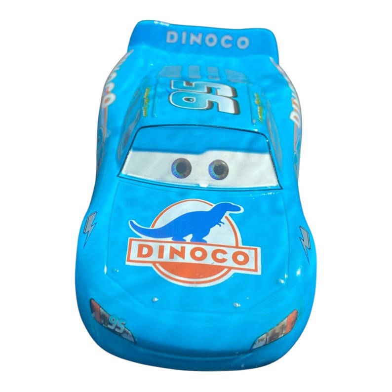 May include: A light blue toy car with the word "DINCO" and the number "95" printed on it. The car has a dinosaur logo and the number "55" on the hood. The car has a white windshield and headlights.