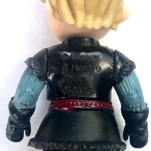 May include: A black and blue plastic action figure of a boy with blonde hair. The figure is wearing a black vest, a red belt, and black pants. The figure is wearing black gloves and has a blue and white sleeve on one arm. The figure has the text "Disney Hasbro China E-031G" printed on the back.