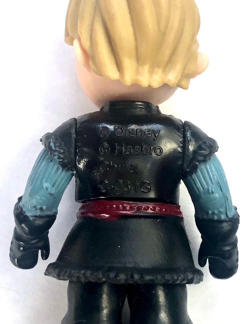 May include: A black and blue plastic action figure of a boy with blonde hair. The figure is wearing a black vest, a red belt, and black pants. The figure is wearing black gloves and has a blue and white sleeve on one arm. The figure has the text "Disney Hasbro China E-031G" printed on the back.