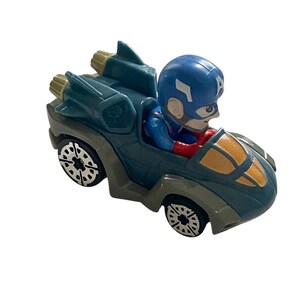 May include: A toy car featuring Captain America in a blue helmet and suit. The car is primarily teal with gold accents and black wheels. The car has a jet-like design with two gold exhaust pipes.