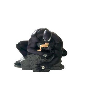 May include: Black and gray figurine of Venom, a Marvel Comics superhero, crouching on a gray base. The figurine is detailed with a black suit and a white spider symbol on the chest.