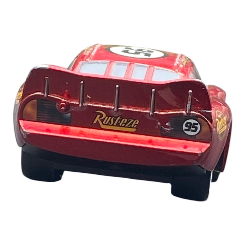 Peut inclure: Une voiture de course jouet rouge avec le num&eacute;ro 95 sur le c&ocirc;t&eacute; et un aileron. La voiture porte l'inscription "Rusteze" &agrave; l'arri&egrave;re. Il s'agit d'un jouet de collection.