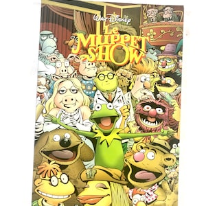 May include: A comic book cover featuring the Muppets from the Muppet Show. The cover is yellow, red and green with the title "The Muppet Show" in large, bold letters. The characters are all smiling and looking at the viewer. The text "Le Spectacle Continue" is at the bottom of the cover.