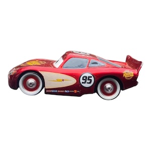 Peut inclure: Une voiture de course jouet rouge avec des pneus &agrave; flancs blancs. La voiture porte le num&eacute;ro 95 sur le c&ocirc;t&eacute; et un motif d'&eacute;clair. Elle a un aileron et le mot "Rusteze" est visible &agrave; l'arri&egrave;re.