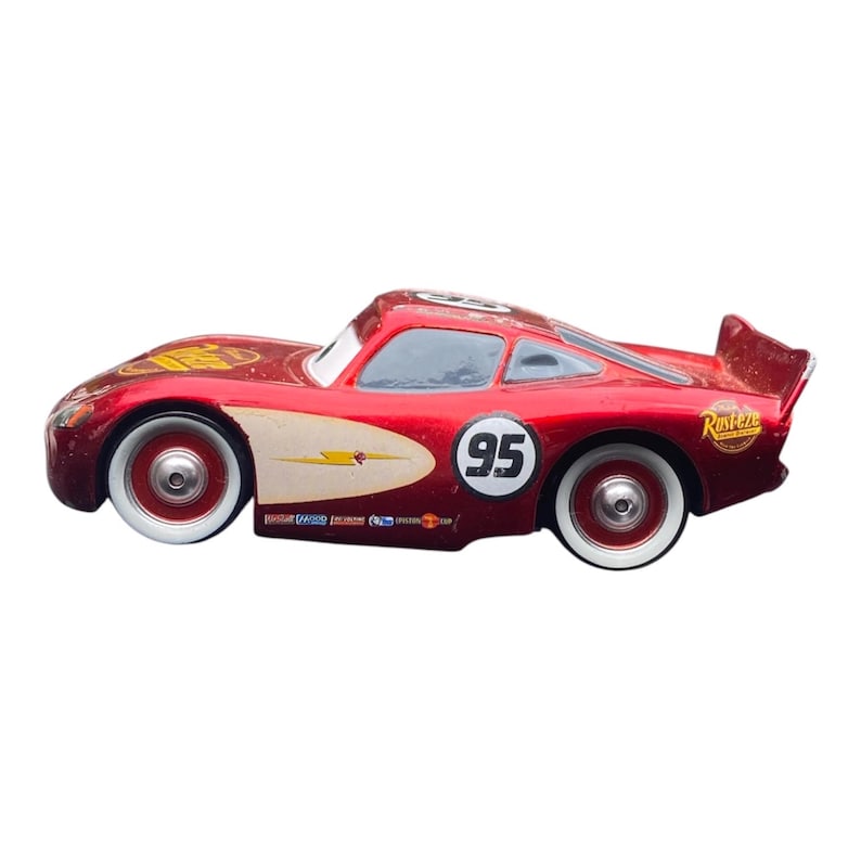 Peut inclure: Une voiture de course jouet rouge avec des pneus &agrave; flancs blancs. La voiture porte le num&eacute;ro 95 sur le c&ocirc;t&eacute; et un motif d'&eacute;clair. Elle a un aileron et le mot "Rusteze" est visible &agrave; l'arri&egrave;re.