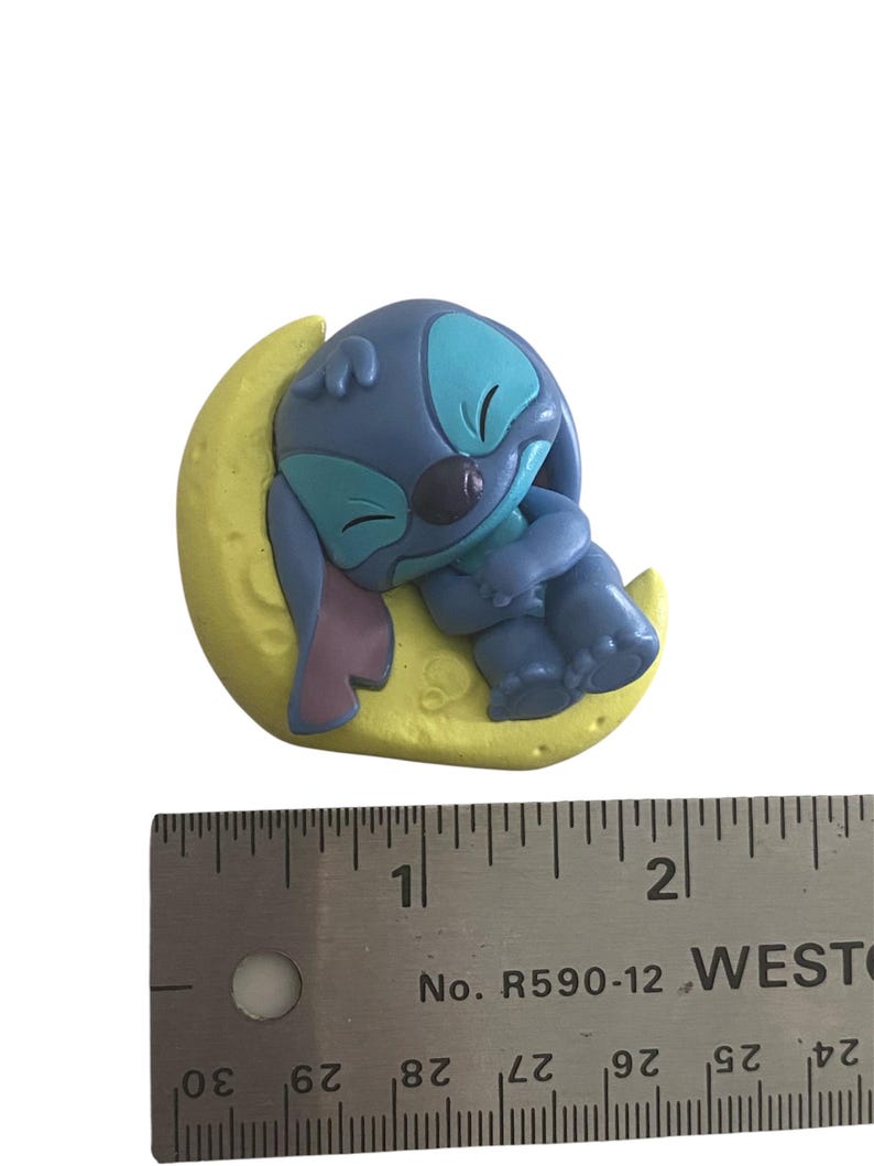 K&ouml;nnte beinhalten: Eine blaue Zeichentrickfigur, die auf einem gelben Halbmond schl&auml;ft. Die Figur hat gro&szlig;e Ohren, einen runden Kopf und umarmt ihre Knie. Der Mond ist strukturiert und hat eine kleine Herzform. Ein Lineal befindet sich neben der Figur.