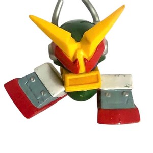 May include: A green, yellow and red plastic toy robot with a yellow helmet and a red visor. The robot has two arms that are extended out to the sides.