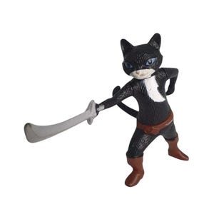 Op de afbeelding: Een zwart kattenbeeldje met een witte borstvlek, bruine riem en laarzen, met een zilveren zwaard. De kat heeft blauwe ogen en een wit masker. Het beeldje staat in een vechthouding.