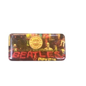 May include: A rectangular pin badge featuring the Beatles' "Sgt. Pepper's Lonely Hearts Club Band" album cover. The badge has a glossy finish and displays the band's name in red lettering. The background is a colourful collage of figures.