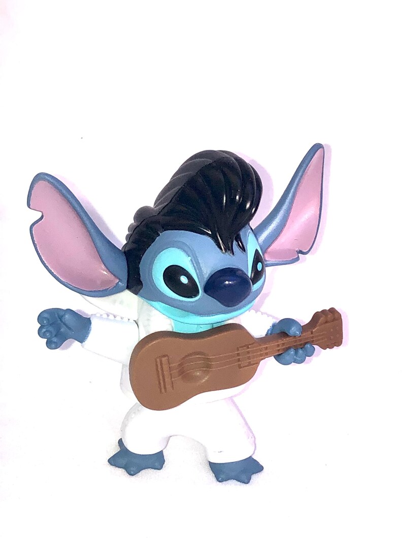 May include: Blue Stitch character with black hair, wearing a white jumpsuit and playing a brown ukulele.