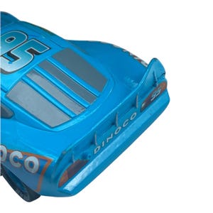 May include: A close-up of a blue toy race car with the number 95 on the side. The car has a Dinoco logo and a spoiler. The car is a vibrant shade of blue with gray and orange accents.
