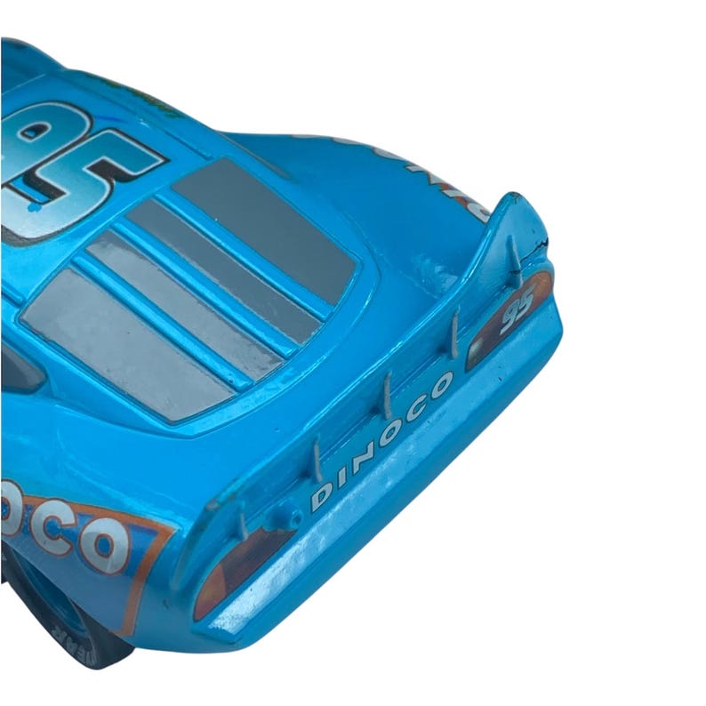 May include: A close-up of a blue toy race car with the number 95 on the side. The car has a Dinoco logo and a spoiler. The car is a vibrant shade of blue with gray and orange accents.