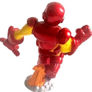 以下が含まれることがあります： 赤いと黄色のアイアンマンのアクションフィギュアがジェットパックで飛んでいます。フィギュアは、片腕を伸ばし、もう片方の手でリパルサービームを持っている、ダイナミックなポーズをとっています。