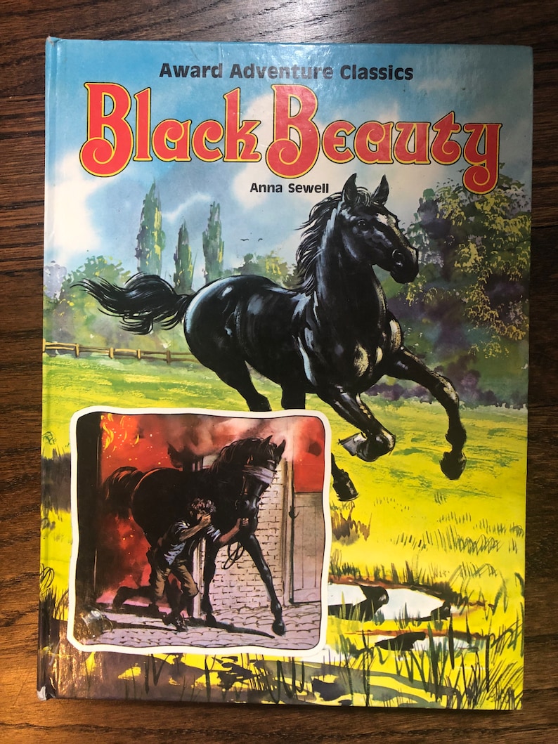 May include: A vintage paperback book cover featuring a black horse running through a field. The title "Black Beauty" is in large red letters with the author "Anna Sewell" below. The cover also includes a smaller image of a horse being led through a burning building.