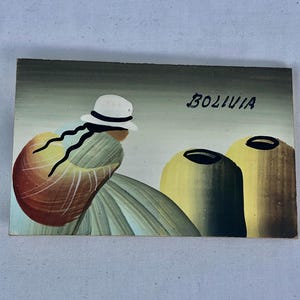 May include: A painting depicting a woman wearing a white hat and carrying a basket on her back. The woman is standing in front of two large, yellow pots. The painting is signed "Bolivia".