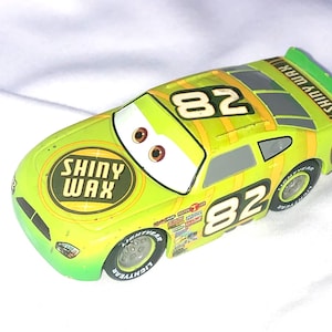 May include: A green toy car with the number 82 on the side. The car has a yellow stripe and the words "Shiny Wax" on the side. The car has a cartoon face with large eyes.