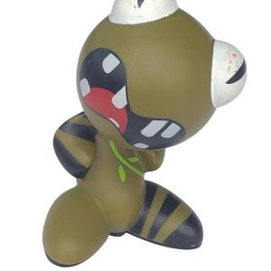 Puede incluir: Un juguete de personaje de dibujos animados verde y negro con la boca muy abierta y ojos grandes. El juguete tiene un diseño de hoja verde en su cuerpo y rayas negras en sus piernas.