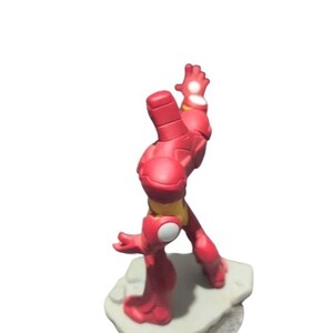 Puede incluir: Figurilla de Iron Man roja y amarilla con un brazo levantado, de pie sobre una base gris.