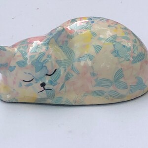 May include: A ceramic sleeping cat figurine with a white base and a blue and pink floral pattern.