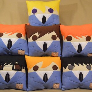 May include: Eight plush pillows featuring characters from the anime Ouran High School Host Club. Each pillow is blue with a white collar and tie, and features a different character's hair and facial features. The pillows are arranged in two rows of four.