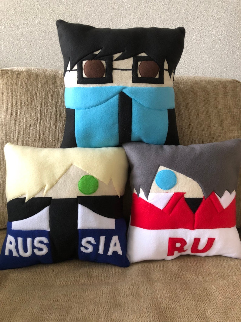May include: Four plush pillows with cartoon faces and text. The pillows are black, white, grey, and yellow with red, blue, and green accents. The text on the pillows reads "RUSSIA" and "RU".