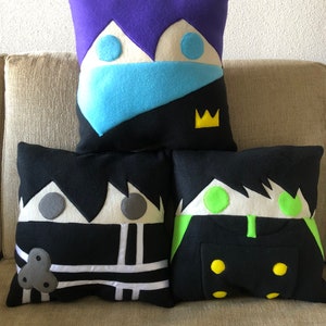 May include: Three decorative pillows with cartoon faces. The pillows are black, white, purple, blue, green, and yellow.
