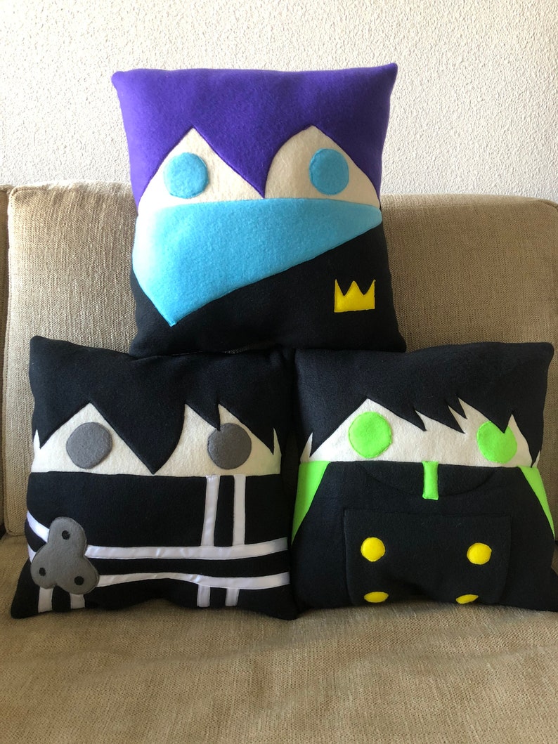 May include: Three decorative pillows with cartoon faces. The pillows are black, white, purple, blue, green, and yellow.