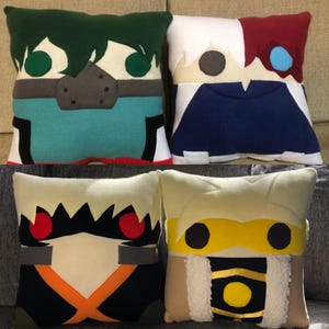 May include: Four plush pillows featuring characters from the anime My Hero Academia. The pillows are green, white, blue, and yellow with black, red, and white details. The characters are Izuku Midoriya, Shoto Todoroki, Katsuki Bakugo, and Eijiro Kirishima.
