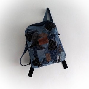 Könnte beinhalten: Ein blauer Jeans-Rucksack aus Patchwork-Stoff. Der Rucksack hat ein braunes Leder-Patch mit dem Wort "Genuine" darauf.