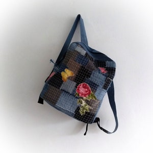 Puede incluir: Una mochila de mezclilla azul con un diseño de patchwork que presenta una rosa, mariposas y un patrón de cuadrícula.
