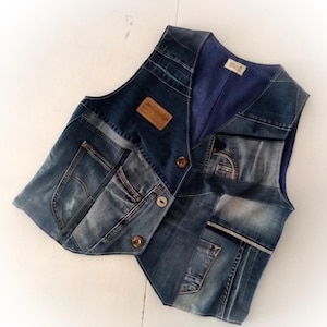 Puede incluir: Un chaleco vaquero patchwork en varios tonos de azul. El chaleco presenta múltiples bolsillos, botones marrones y un forro a rayas azules. Un parche de cuero marrón está cosido en la parte delantera. El chaleco está hecho de mezclilla reciclada.