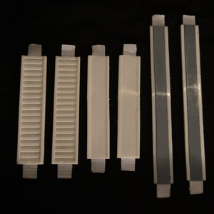 May include: A collection of six white plastic blind slats with fabric straps. Some slats have a slatted design, while others are solid. Two slats have a gray adhesive strip running down the center.