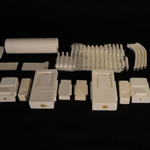 May include: An assortment of white ceramic pieces, including rectangular and cylindrical shapes, arranged against a black background. The collection features various sizes and designs, suggesting components for a larger structure or project.