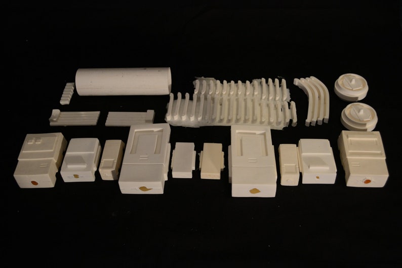 May include: An assortment of white ceramic pieces, including rectangular and cylindrical shapes, arranged against a black background. The collection features various sizes and designs, suggesting components for a larger structure or project.