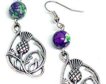 May include: Silver earrings with a purple and green floral design and a silver thistle charm.