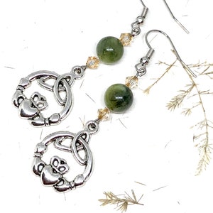 May include: Silver Celtic knot earrings with green and clear beads. The earrings feature a Claddagh design with a heart, hands, and crown.