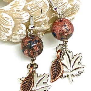 May include: A pair of dangle earrings featuring a brown and red speckled stone with a silver and copper leaf charm.
