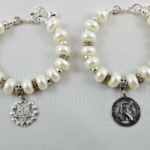 May include: Two white pearl bracelets with silver charms. One charm features a pentagram and the other a stylized Egyptian head.