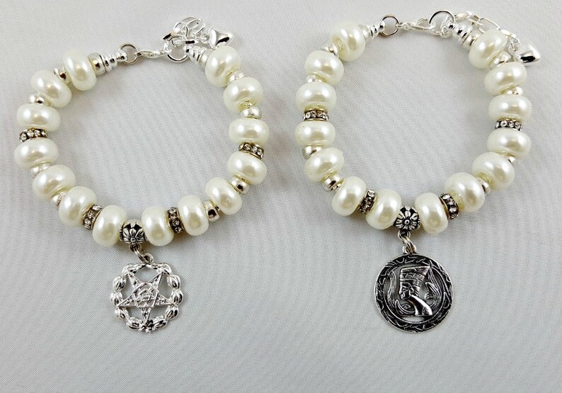 May include: Two white pearl bracelets with silver charms. One charm features a pentagram and the other a stylized Egyptian head.