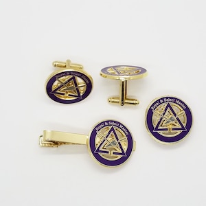 Puede incluir: Un juego de gemelos y pasador de corbata de color dorado con un diseño de esmalte morado con un triángulo y espadas cruzadas. El diseño incluye el texto "Royal & Select Master".