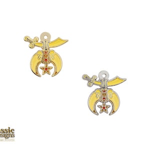 May include: Two gold-toned metal charms featuring a crescent moon and star with a sword and a red star in the center. The charms are on a white background.
