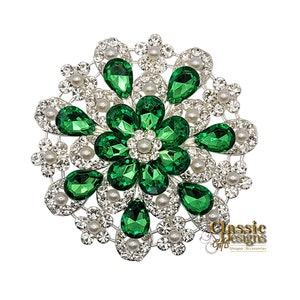 Puede incluir: Un broche grande de color verde y plateado con un diseño de flor. El broche está hecho de pedrería y perlas.